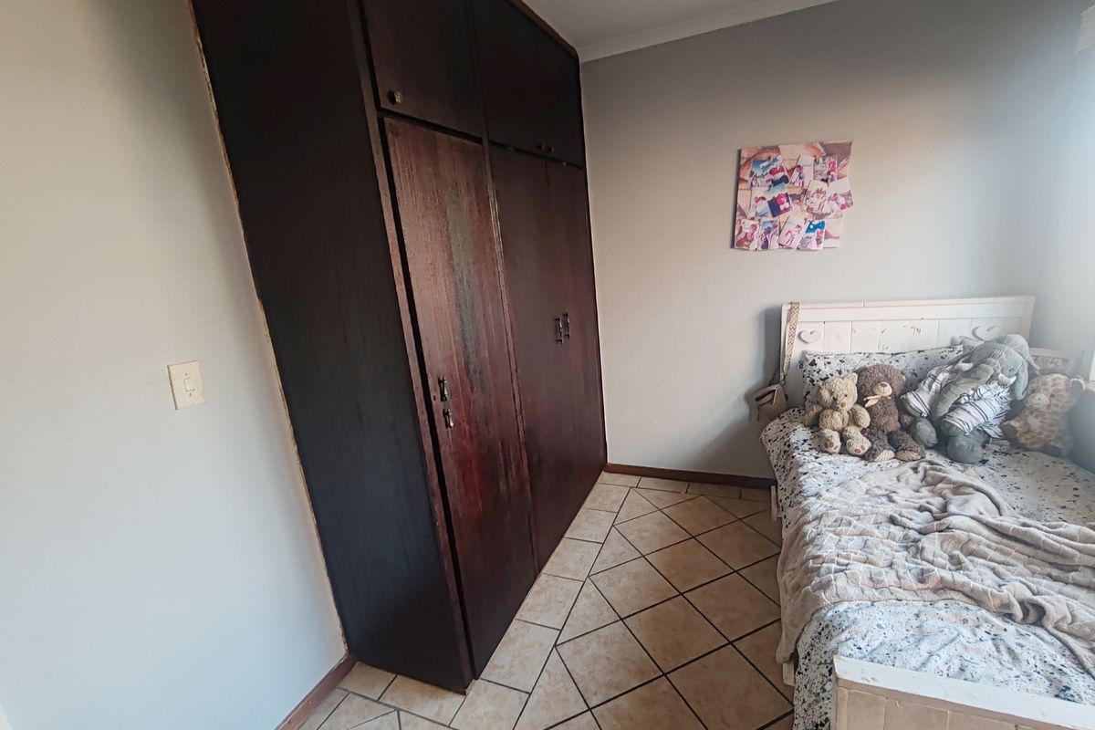 A bedroom featuring dark wood built-in cupboards and tiled flooring, offering a functional space with potential for cosmetic updates.