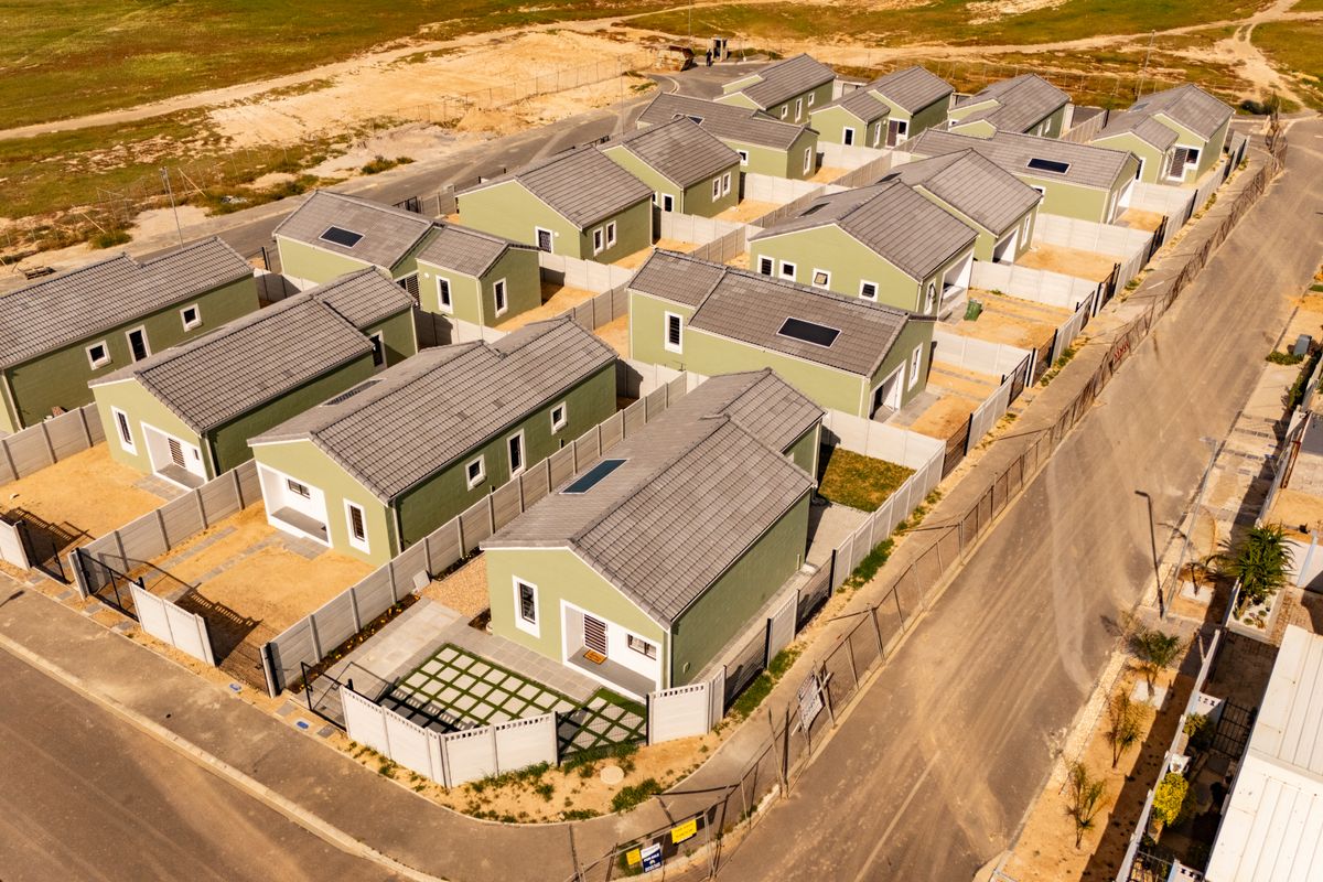 Aerial view of a modern residential housing development featuring uniform detached homes with tiled roofs, solar panels, and enclosed private yards.