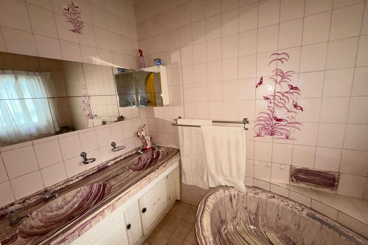 A dated bathroom featuring a dual vanity with integrated stone-look basins, a matching built-in bathtub, and decorative wall tiling.