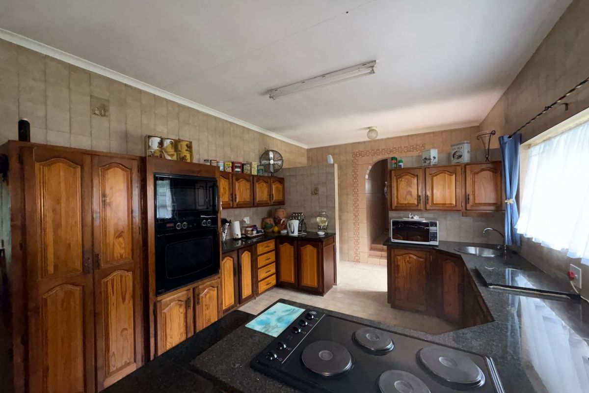 A spacious kitchen featuring extensive wooden cabinetry, granite countertops, built-in oven, and electric hob, offering a functional layout with potential for modern updates.