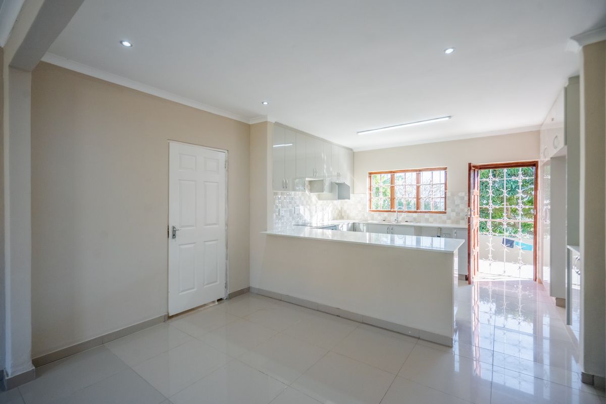 A bright, modern kitchen featuring sleek cabinetry, stone countertops, tiled backsplash, and direct access to the outdoor area through a security gate.
