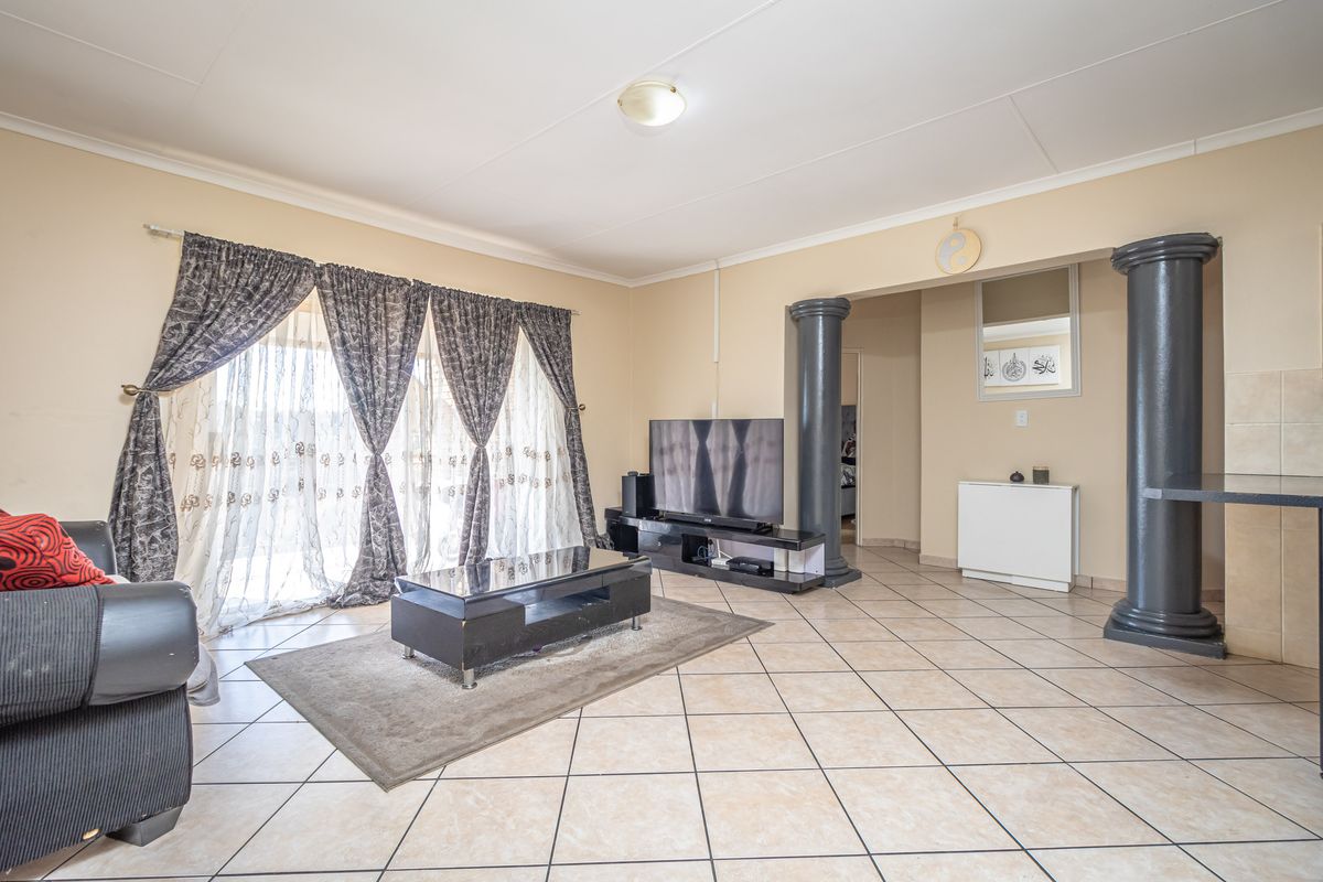 Spacious living area featuring neutral ceramic floor tiles, decorative columns, and large windows with curtains, offering a bright and open living space.