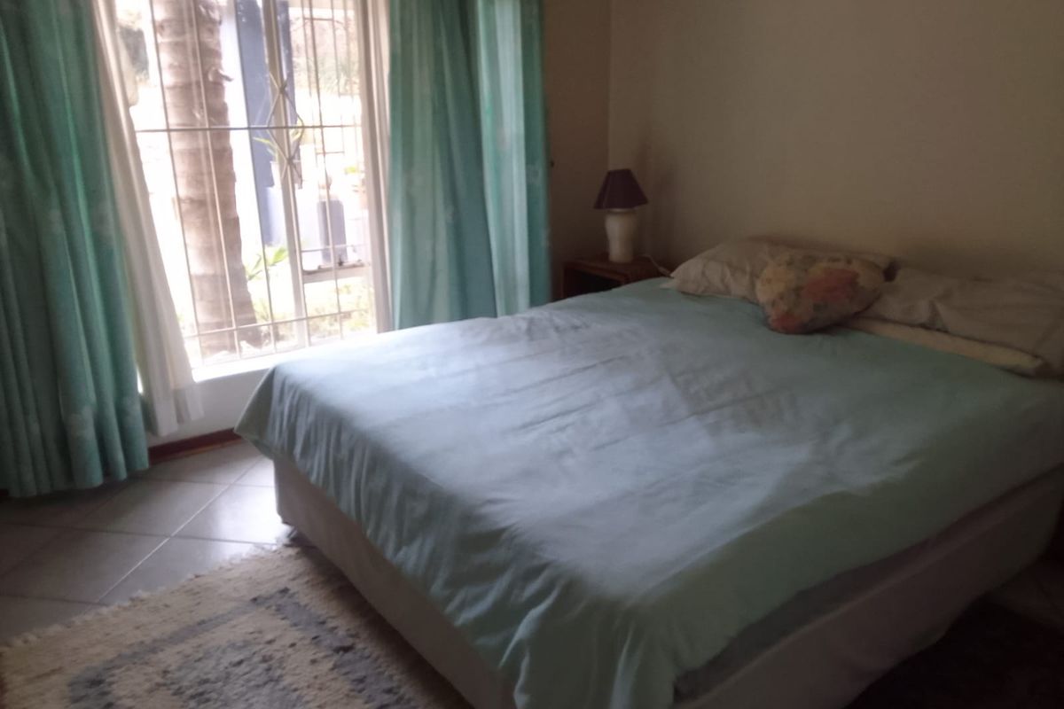 A bedroom featuring tiled flooring and a window fitted with security bars, providing natural light.
