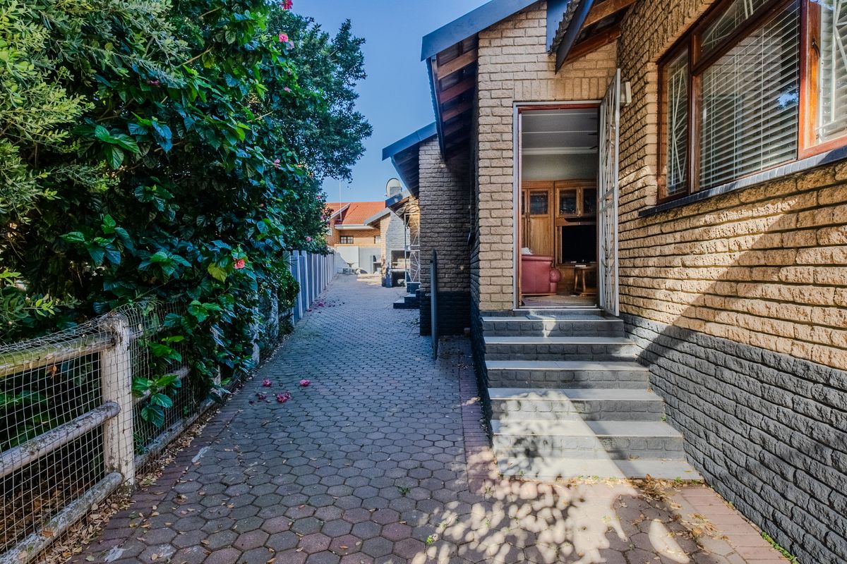 A view of the rear exterior of the house, featuring a paved walkway, brick facade, and access steps leading into the living area.