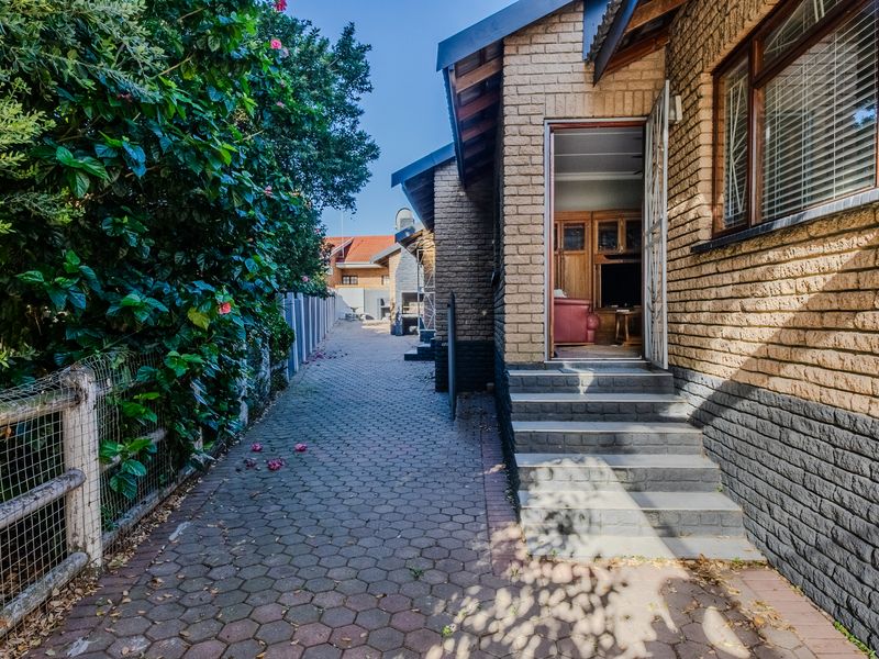 A view of the rear exterior of the house, featuring a paved walkway, brick facade, and access steps leading into the living area.