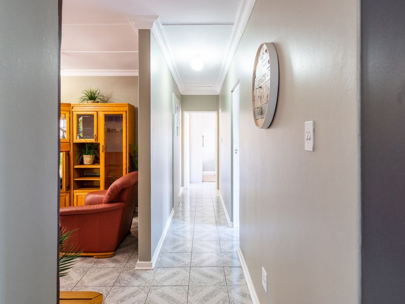A well-lit hallway featuring tiled flooring and crown molding, providing access to adjacent living areas and rooms.