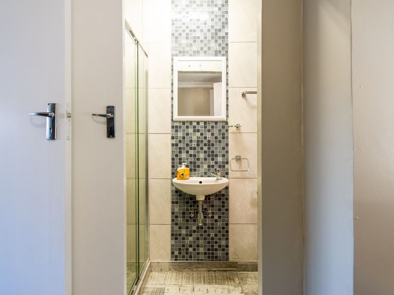 A compact bathroom featuring a wall-mounted basin, a glass shower enclosure, and a decorative mosaic tile feature wall.