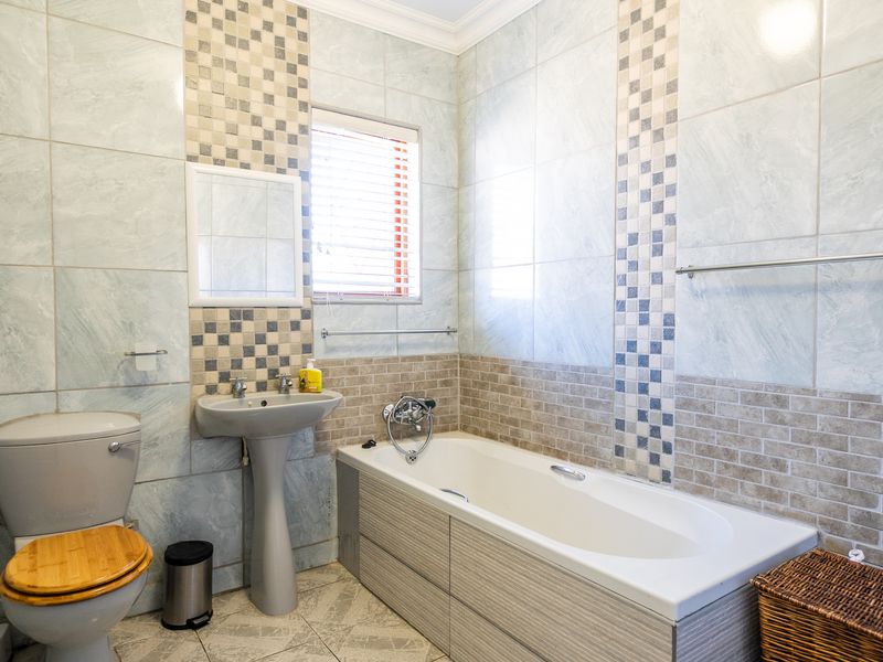 A functional bathroom featuring a pedestal sink, built-in bathtub, and toilet, finished with decorative wall tiling and a window for natural light.