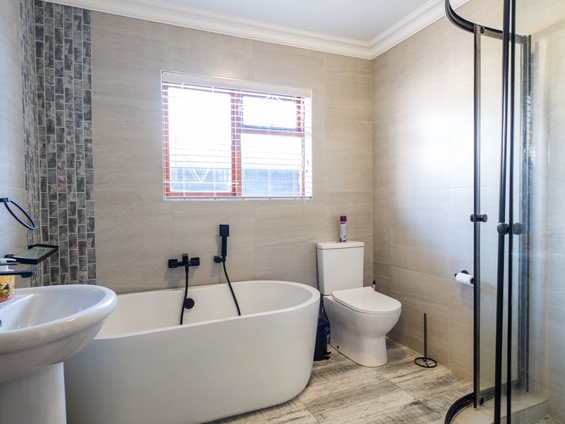 Modern bathroom featuring a freestanding bathtub, walk-in shower with black matte fixtures, and neutral floor-to-ceiling tiling.