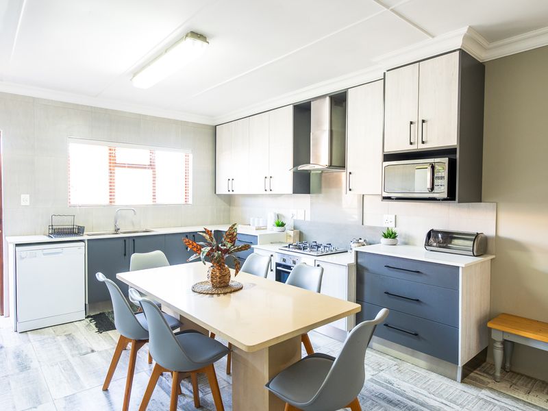 Modern open-plan kitchen featuring two-tone cabinetry, integrated appliances, gas hob, and tiled flooring, seamlessly flowing into a dining area.