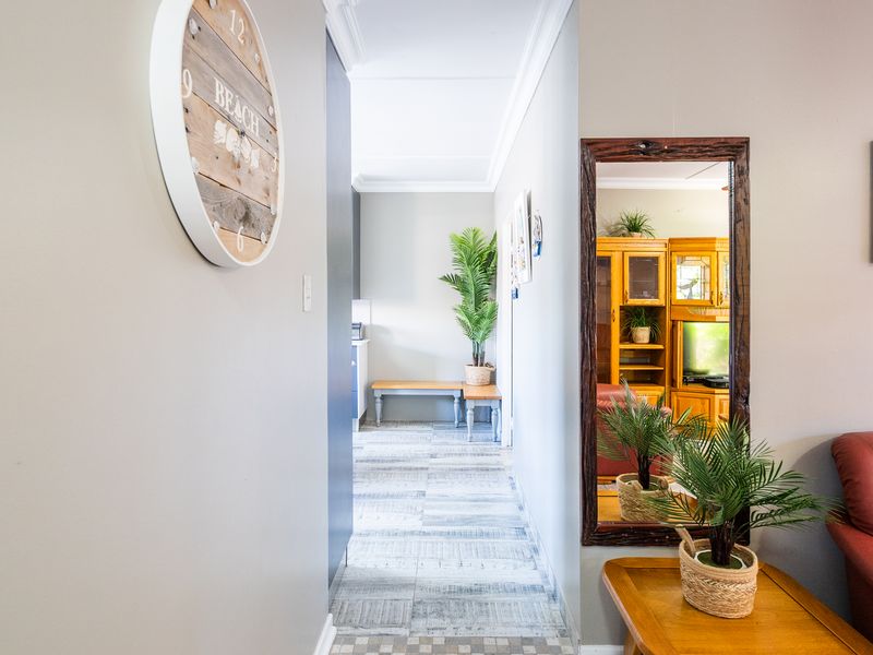 A bright, well-maintained hallway featuring neutral wall tones, decorative cornicing, and patterned tiled flooring leading towards the rear of the home.