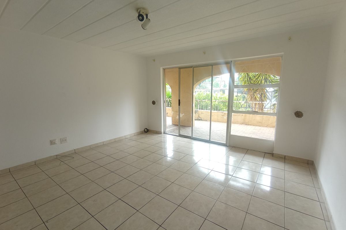 An empty, tiled living room featuring a sliding glass door that opens onto a covered patio area.