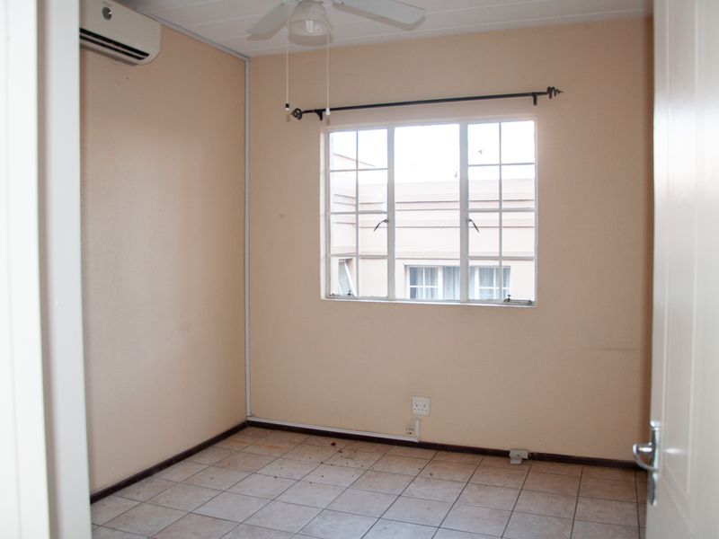 An empty bedroom featuring tiled flooring, a ceiling fan, and a wall-mounted air conditioning unit.