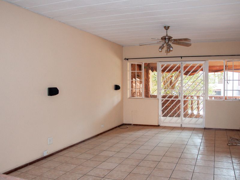 Spacious, empty living area featuring tiled flooring, a ceiling fan, and a secure sliding door leading to an outdoor balcony.