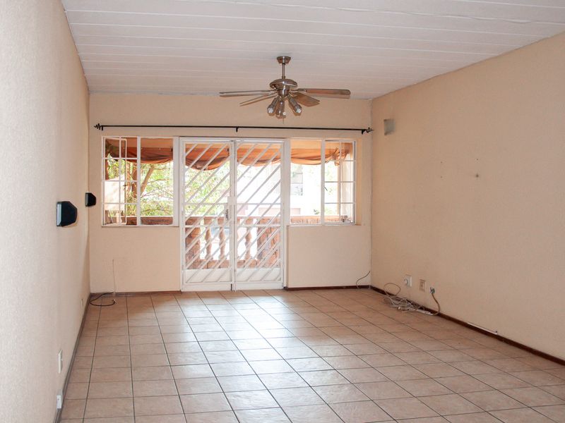 An empty living room featuring tiled flooring, a ceiling fan, and a security gate leading to an outdoor area.