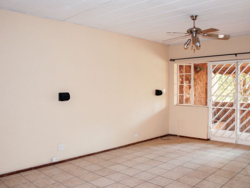 An empty living room featuring tiled flooring, a ceiling fan, and a security gate leading to an outdoor area.