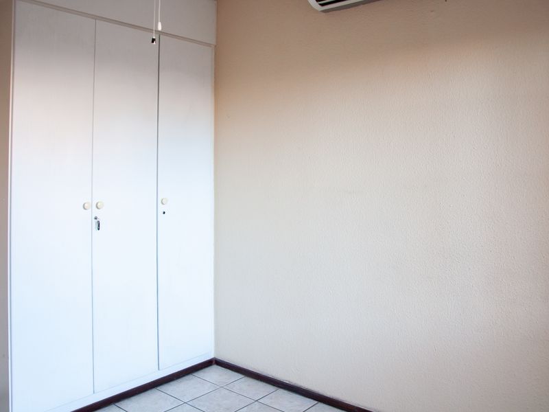 A clean, empty bedroom featuring built-in white cupboards, tiled flooring, and a wall-mounted air conditioning unit.