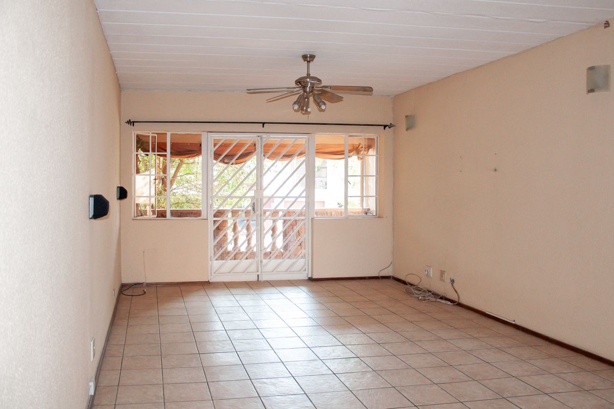 An empty living room featuring tiled flooring, a ceiling fan, and a security gate leading to an outdoor area.
