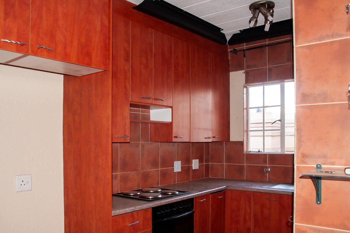 A dated kitchen featuring wood-look cabinetry, a tiled backsplash, and integrated electric cooking appliances, offering potential for a modern renovation.