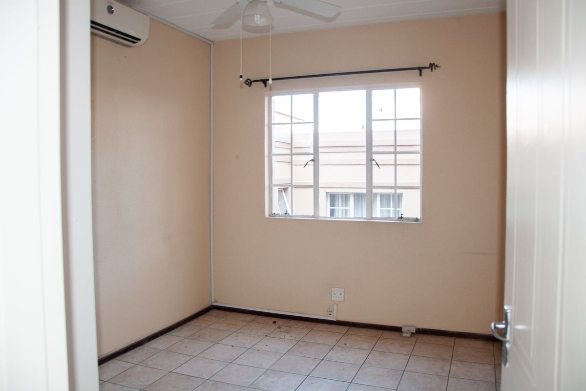 An empty bedroom featuring tiled flooring, a ceiling fan, and a wall-mounted air conditioning unit.