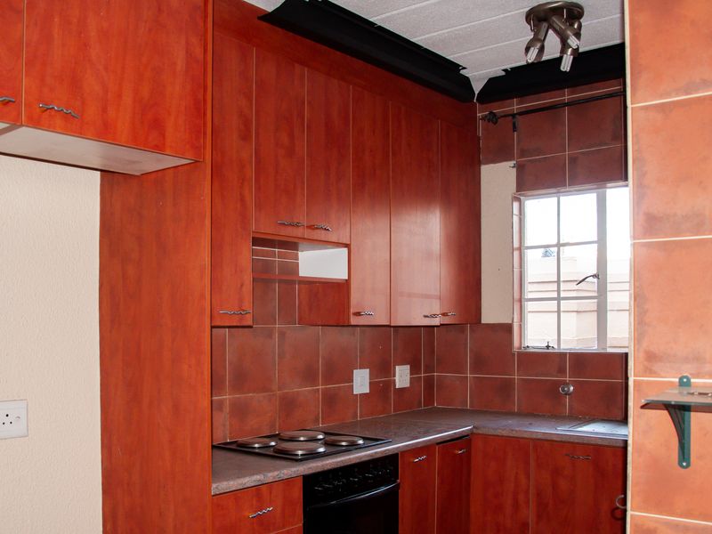 A dated kitchen featuring wood-look cabinetry, a tiled backsplash, and integrated electric cooking appliances, offering potential for a modern renovation.