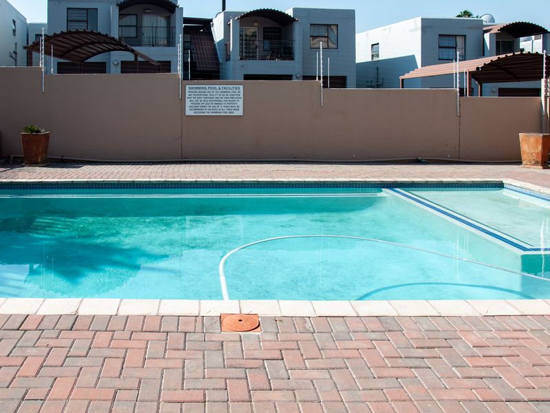 Communal swimming pool area featuring paved decking, perimeter walling with electric fencing, and standard pool infrastructure.