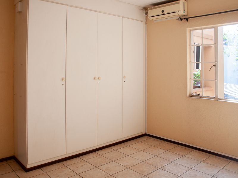 An empty bedroom featuring built-in cupboards, tiled flooring, and a wall-mounted air conditioning unit.