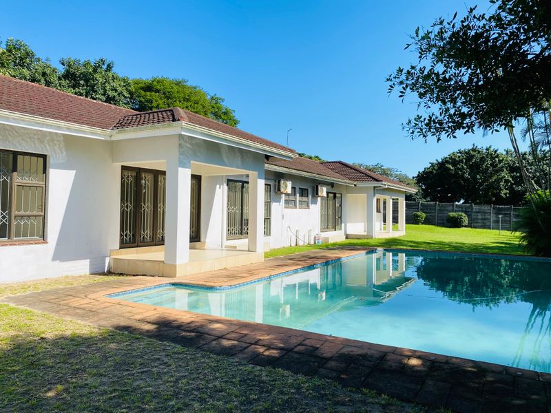 A spacious rear garden featuring a swimming pool, a covered patio area, and direct access to the home through multiple sliding glass doors.