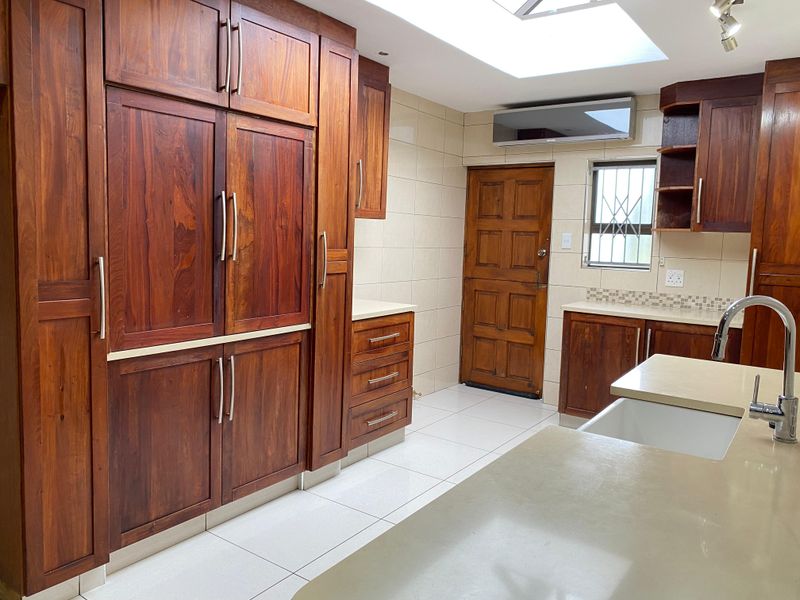 A spacious kitchen featuring solid wood cabinetry, stone countertops, a farmhouse sink, and a large skylight, providing a bright and functional workspace.