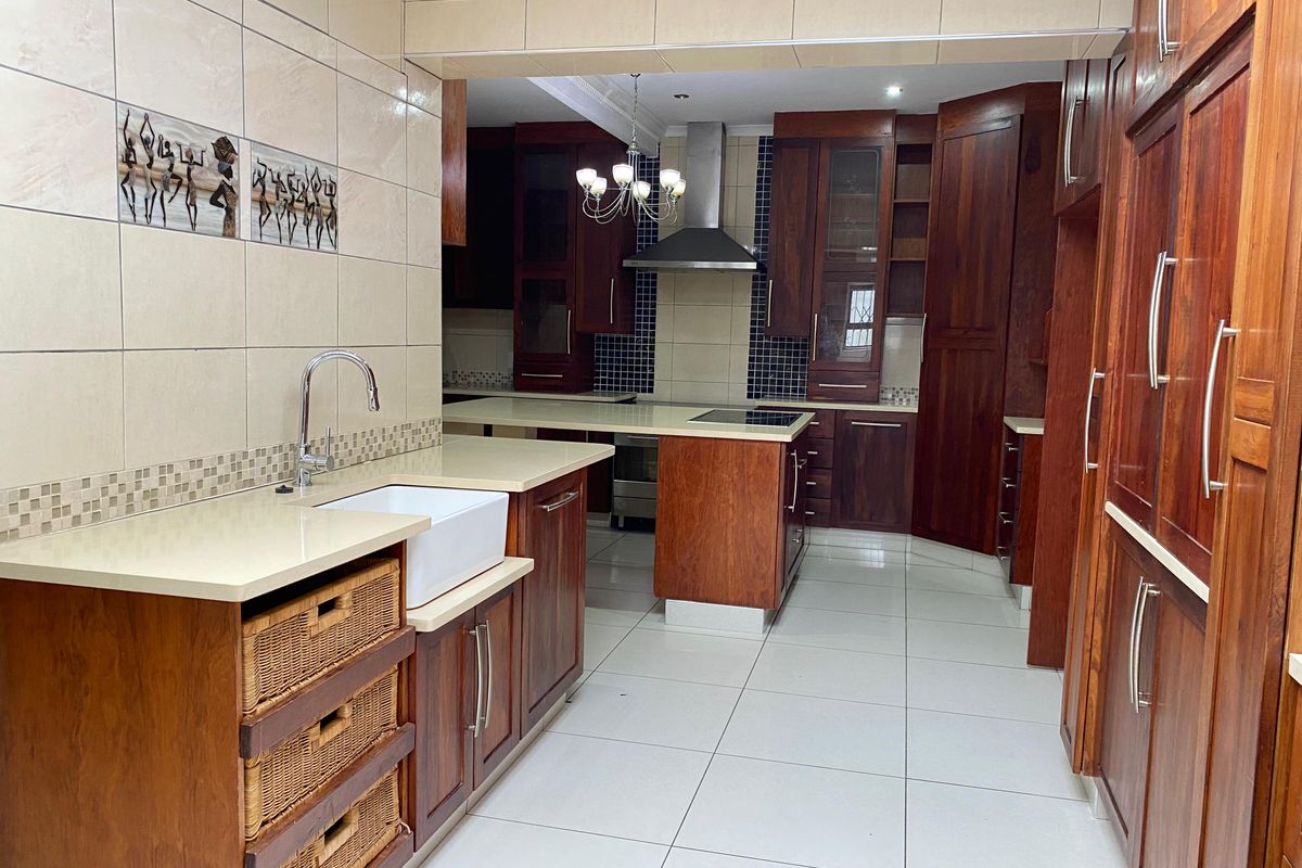 Spacious kitchen featuring rich wooden cabinetry, stone countertops, a farmhouse sink, and integrated stainless steel appliances with modern tiled finishes.