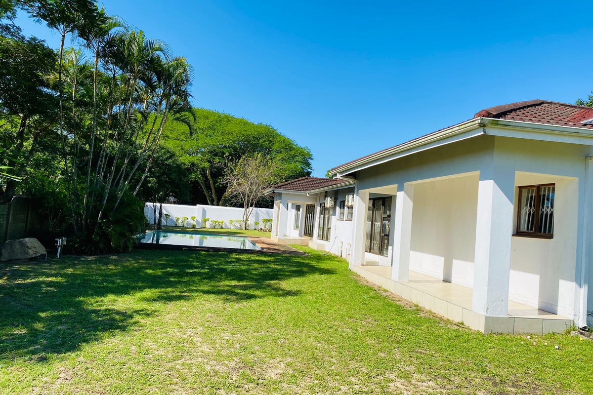 Rear view of the property featuring a covered patio, a swimming pool, and a spacious garden area with established trees and perimeter walling.