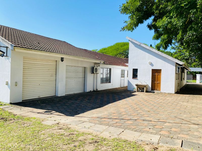 Rear exterior view of the property featuring a double garage with roller shutter doors, paved driveway, and an external wash basin.