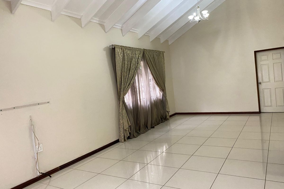 Spacious living area featuring high vaulted ceilings with exposed rafters, neutral tiled flooring, and a classic chandelier, presenting a clean, blank canvas.