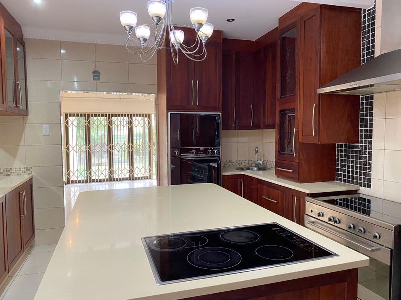 A well-appointed kitchen featuring rich wooden cabinetry, stone countertops, a central island with an integrated cooktop, and modern built-in appliances.