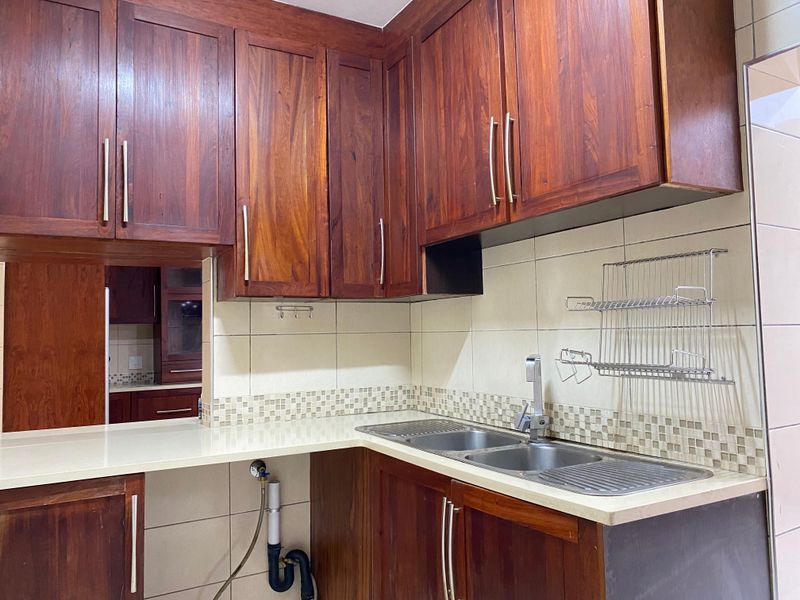 A kitchen area featuring dark wood cabinetry, a double sink with a mixer tap, and tiled backsplash with decorative mosaic accents.
