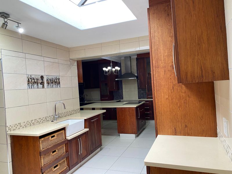 Spacious kitchen featuring warm wood cabinetry, stone countertops, a farmhouse sink, and a large skylight, offering a functional and well-lit culinary workspace.