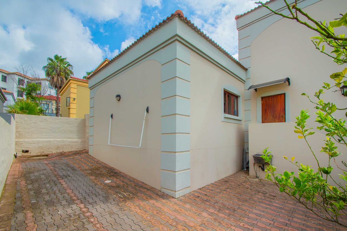 A view of the rear exterior area featuring paved ground, a wall-mounted utility sink, and a side entrance door.