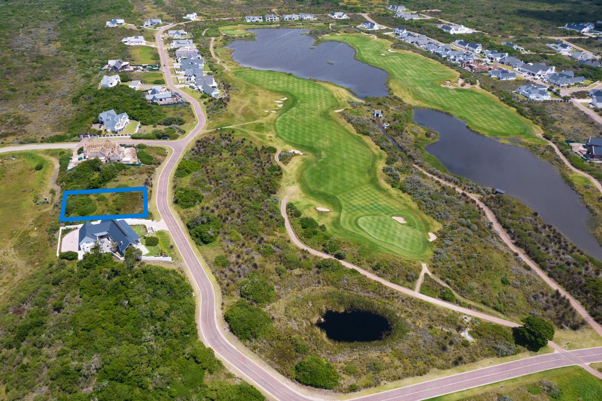 An aerial view of a vacant residential plot situated within a golf estate, featuring surrounding natural landscape and water features.