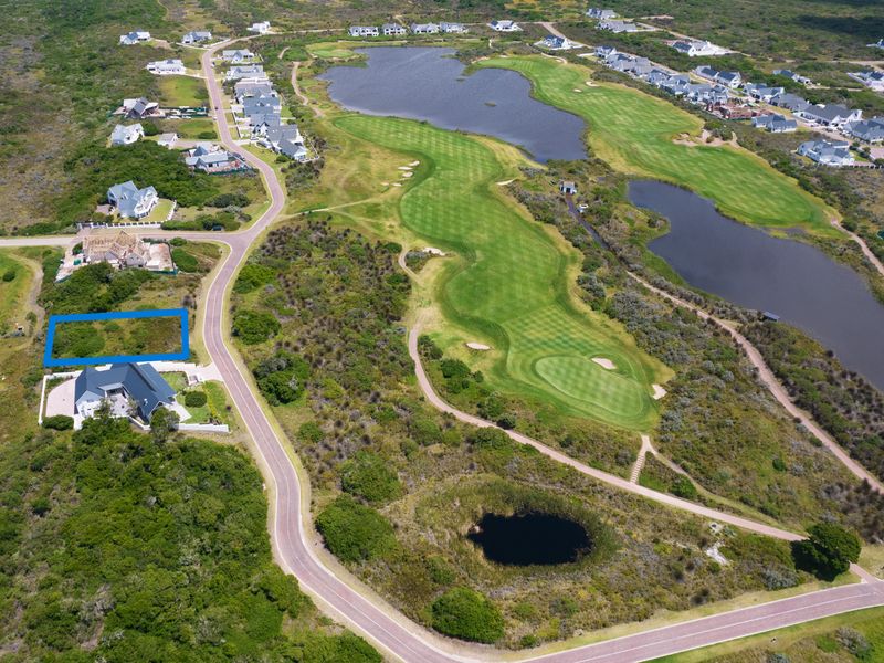 An aerial view of a vacant residential plot situated within a golf estate, featuring surrounding natural landscape and water features.