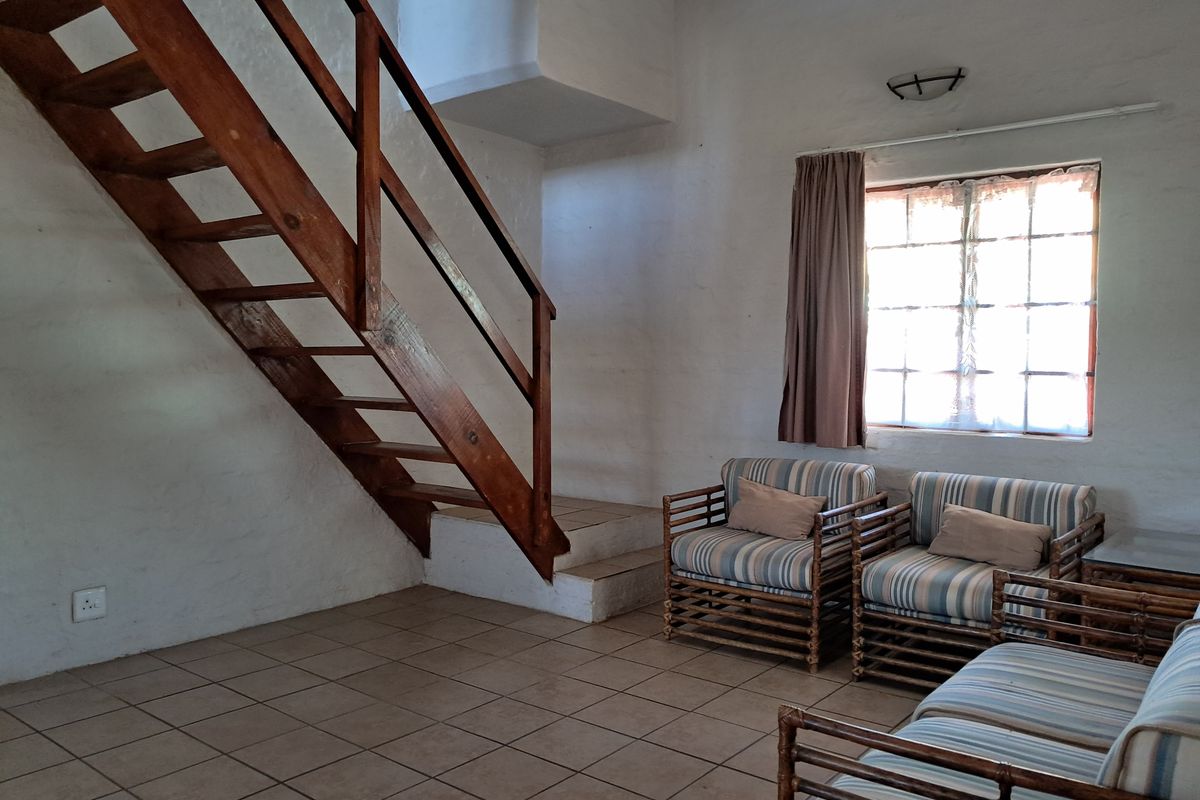 A living room featuring tiled flooring, a wooden staircase, and a multi-pane window, offering a rustic aesthetic with potential for modernization.