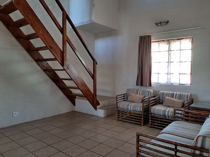 A living room featuring tiled flooring, a wooden staircase, and a multi-pane window, offering a rustic aesthetic with potential for modernization.