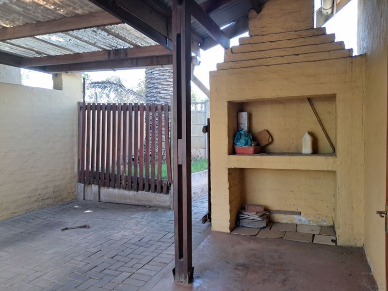 Covered outdoor patio area featuring a built-in braai, paved flooring, and timber structural elements, offering a functional space for outdoor entertainment.