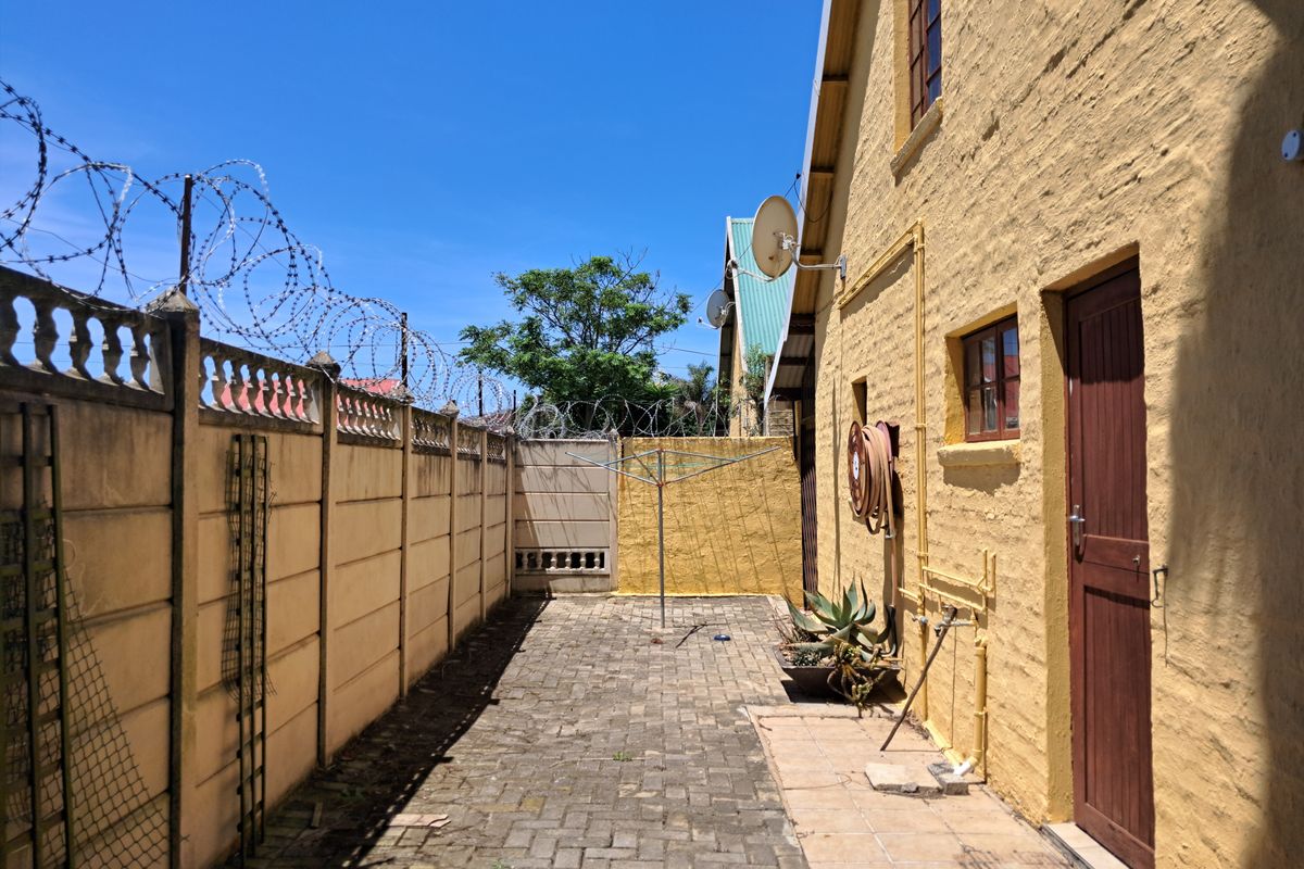 A rear exterior courtyard featuring paved flooring, a precast boundary wall with security razor wire, and direct access to the property via a timber door.