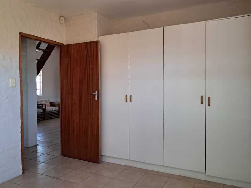 A bedroom featuring built-in cupboards, tiled flooring, and a wooden door, with a view into an adjacent living area.