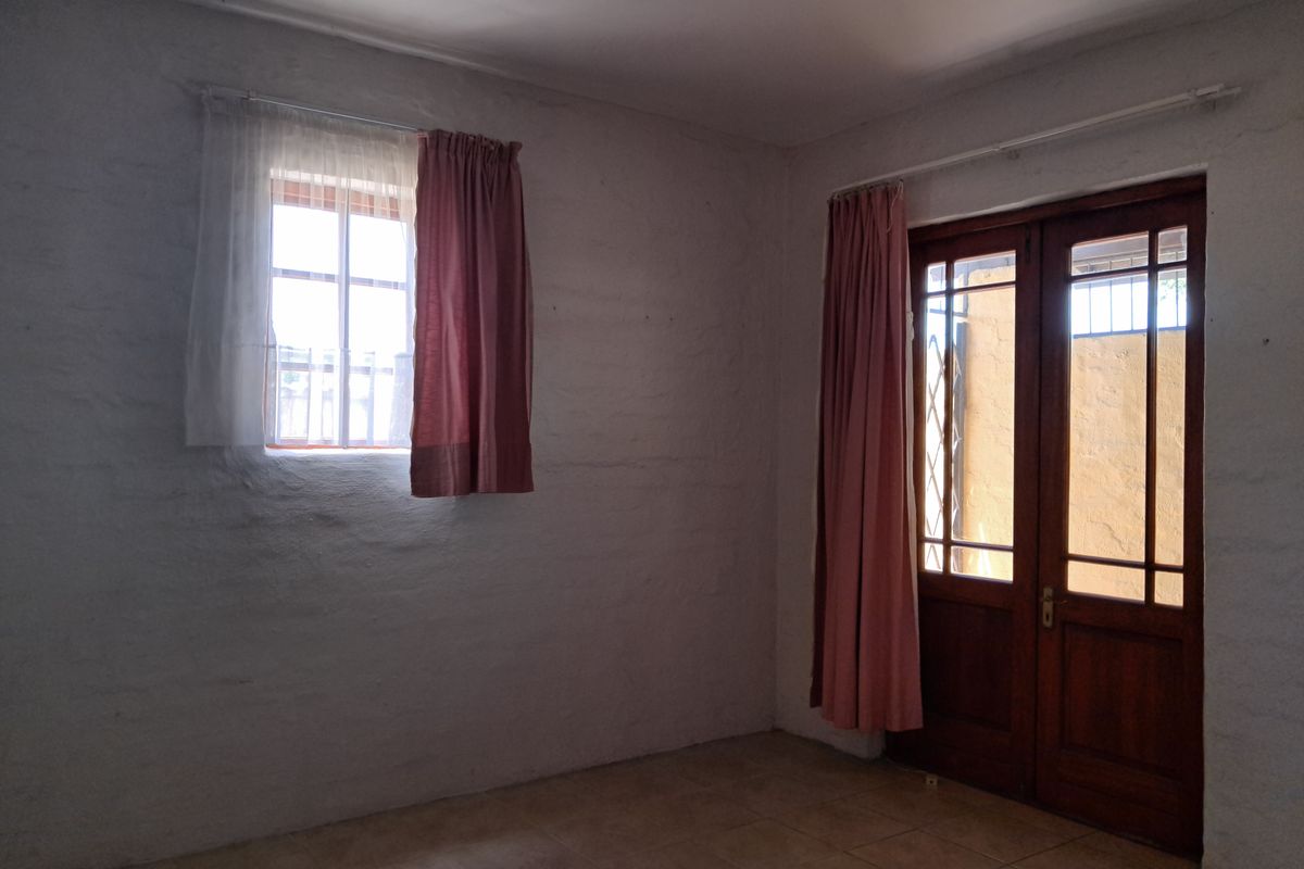 An empty bedroom featuring tiled flooring, a timber-framed glass door leading outside, and a window with security bars.