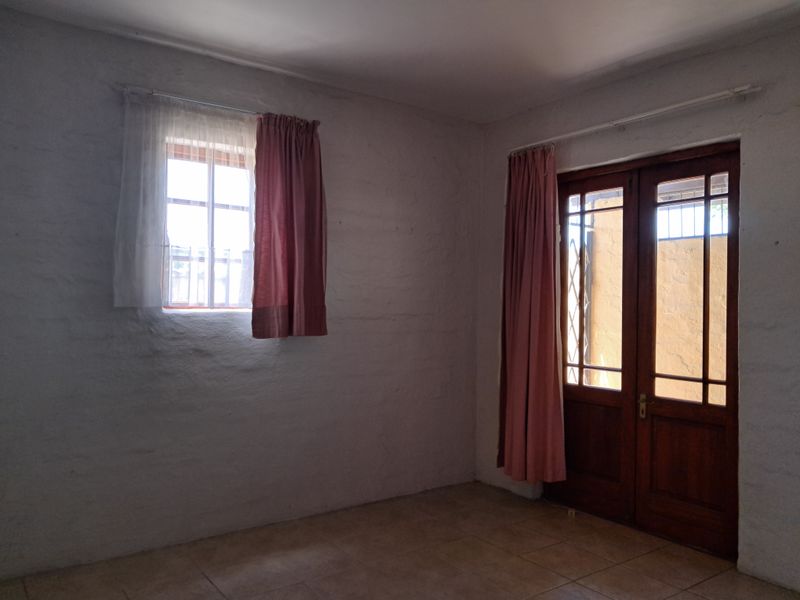 An empty bedroom featuring tiled flooring, a timber-framed glass door leading outside, and a window with security bars.
