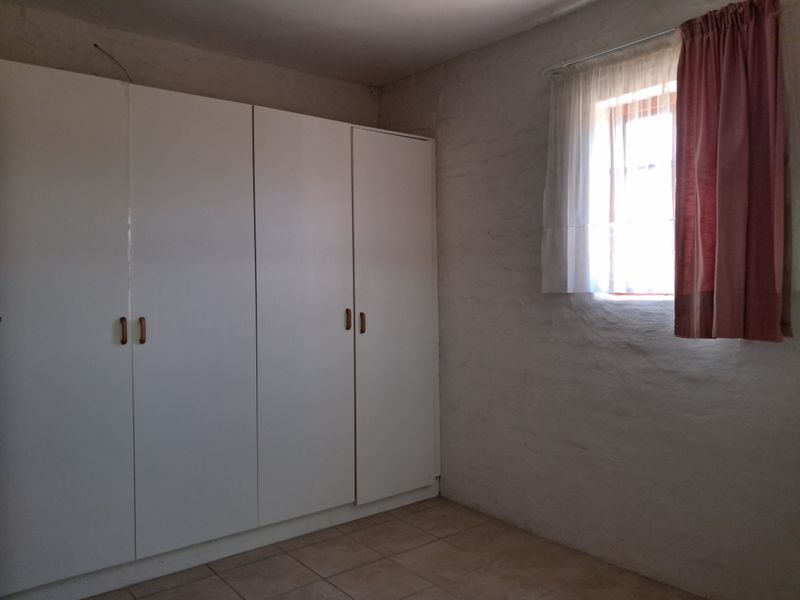 A bedroom featuring built-in wardrobes, tiled flooring, and a window. The room is currently empty and requires cosmetic updates to the wall finishes.