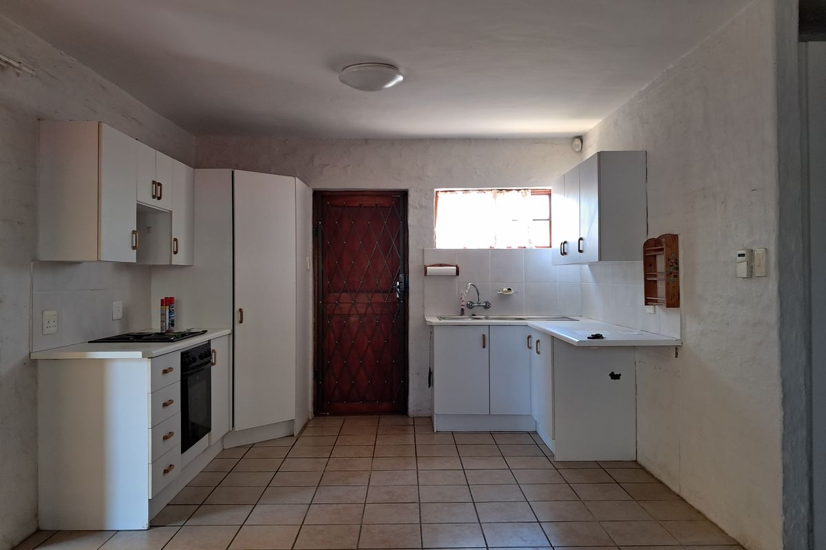 A functional kitchen featuring white built-in cabinetry, a built-in oven, hob, and tiled flooring, with a security gate leading to the exterior.