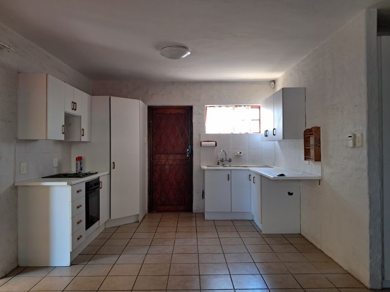 A functional kitchen featuring white built-in cabinetry, a built-in oven, hob, and tiled flooring, with a security gate leading to the exterior.