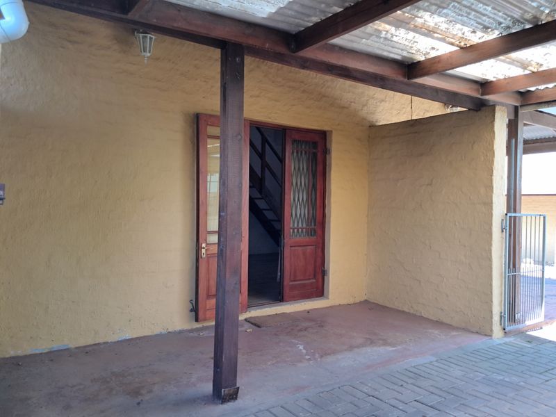 A covered outdoor patio area featuring a timber pergola structure, paved flooring, and double timber doors leading into the property.
